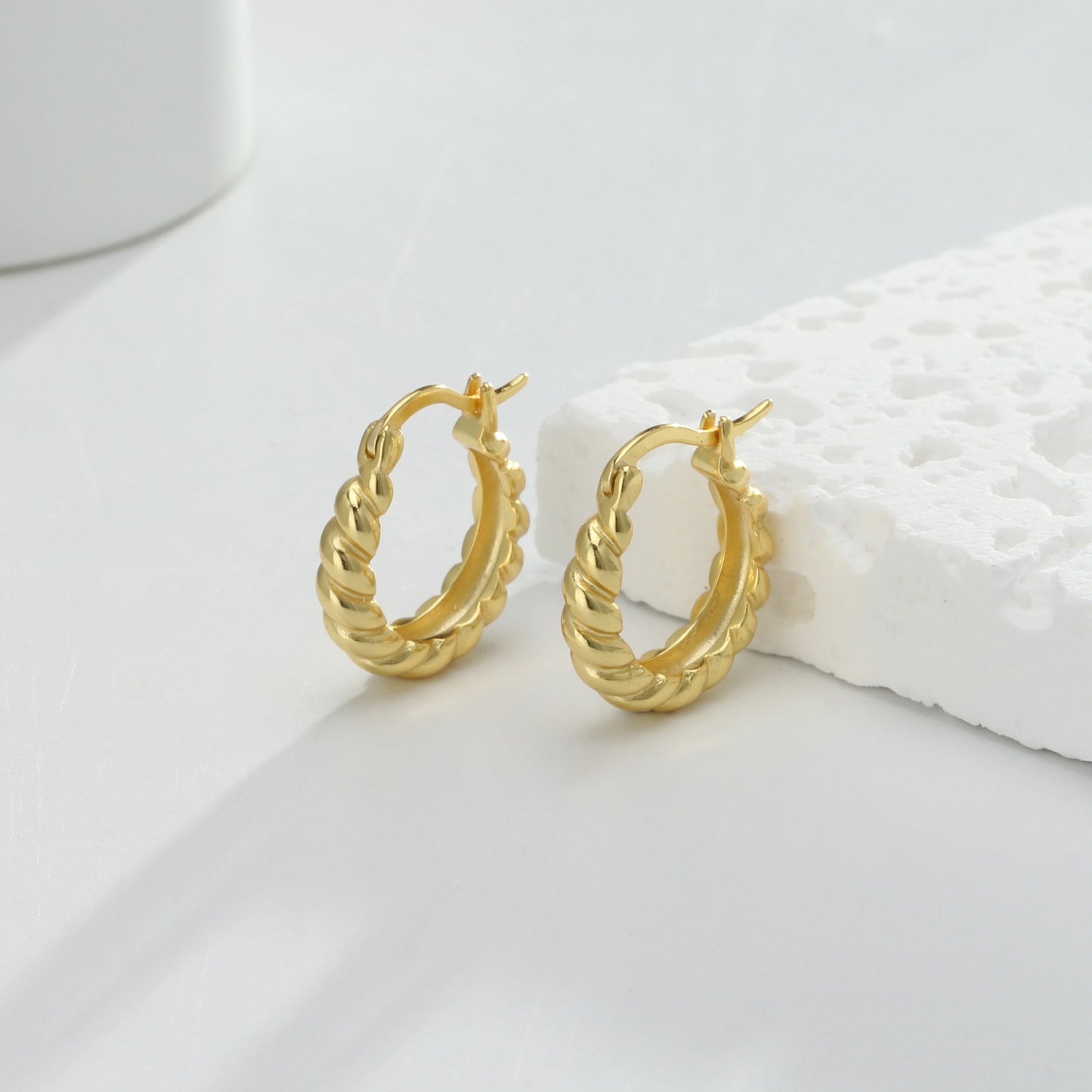 une paire de boucles d'oreilles en or sur une surface blanche