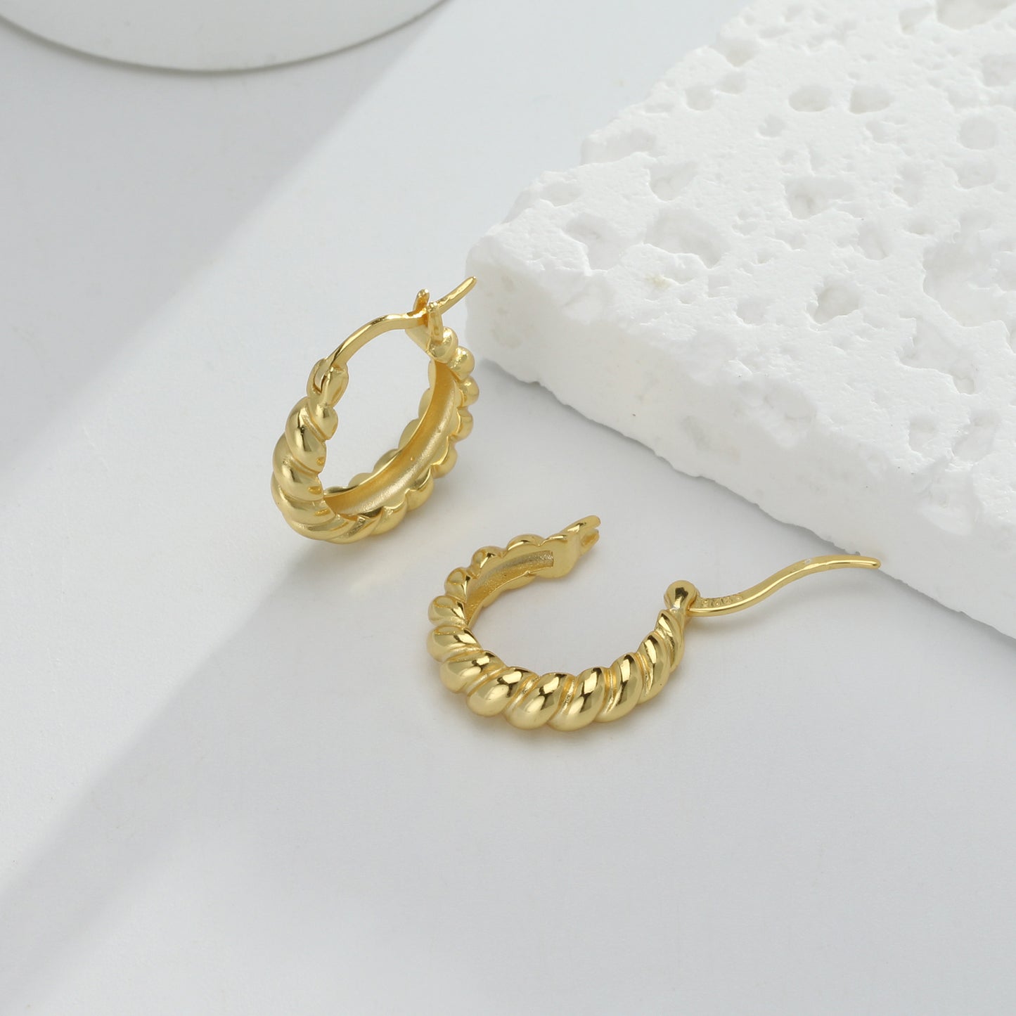 une paire de boucles d'oreilles en or sur une surface blanche