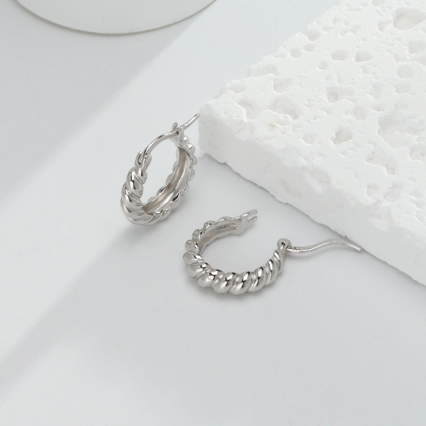 une paire de boucles d'oreilles en argent posée sur une surface blanche