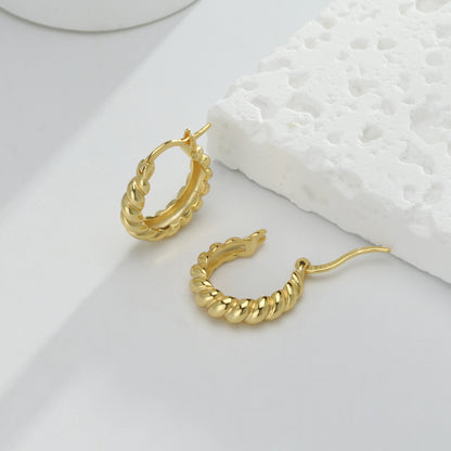 une paire de boucles d'oreilles en or sur une surface blanche