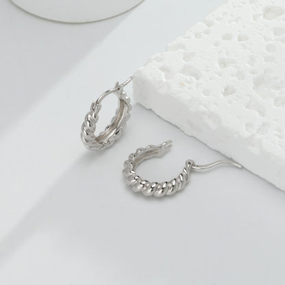 une paire de boucles d'oreilles en argent posée sur une surface blanche